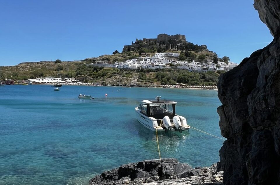 My dolce vita yacht is anchored in clear blue water of Lindos bay. In the background the all white scenic town of Lindos